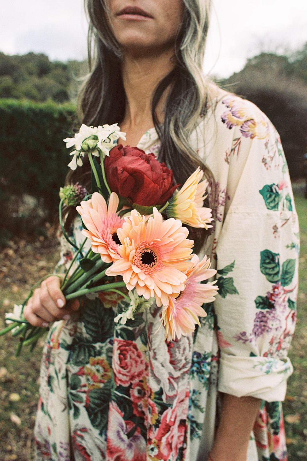 Model holding flowers wearing a Metta Melbourne 'Paloma Dress in Bouquet Print' floral dress. 
