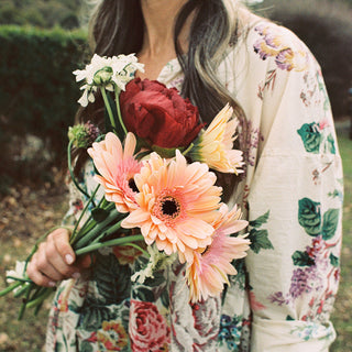 Model holding flowers wearing a Metta Melbourne 'Paloma Dress in Bouquet Print' floral dress. 